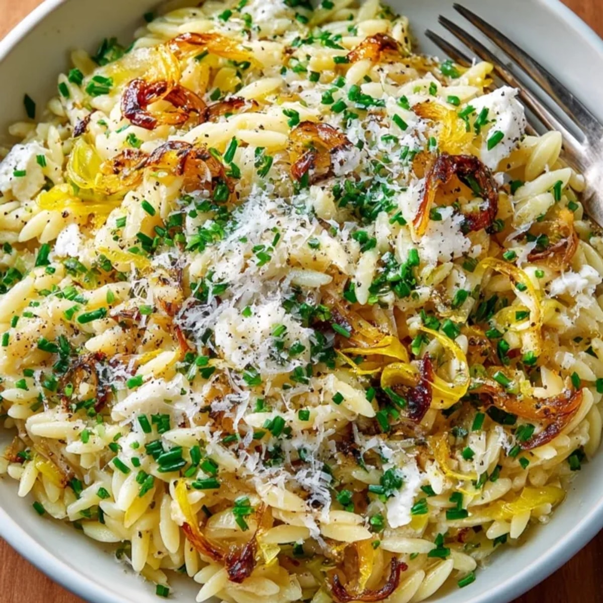 Creamy Orzo with Caramelized Onions and Goat Cheese, ready to serve, topped with herbs.