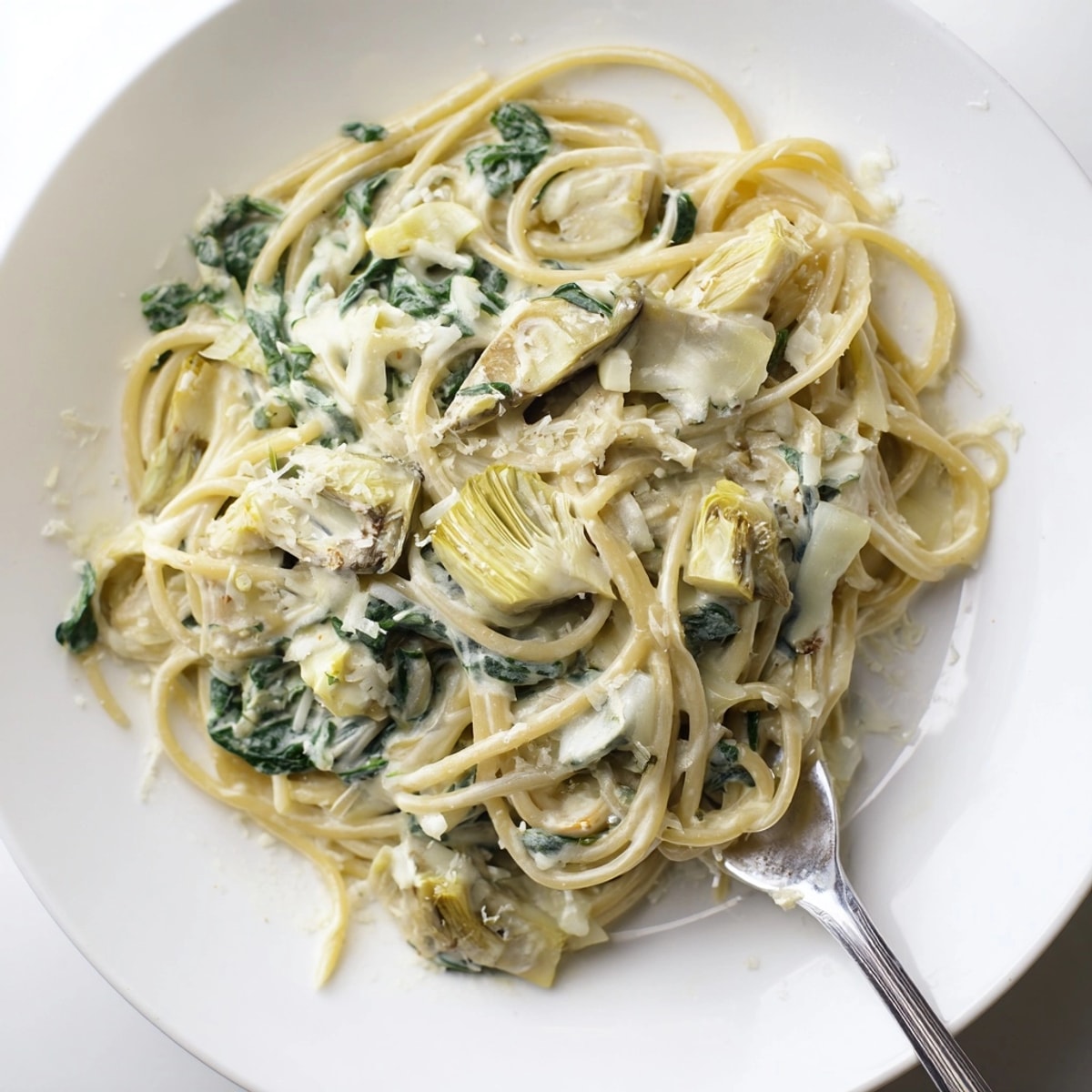 Creamy Spinach Artichoke Spaghetti, a bubbling skillet of pasta in rich, cheesy sauce.