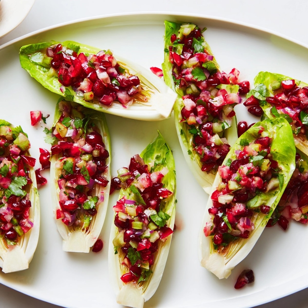 Close up of festive Cranberry Jalape&ntilde;o Salsa Boats, endive leaves brimming with red relish.