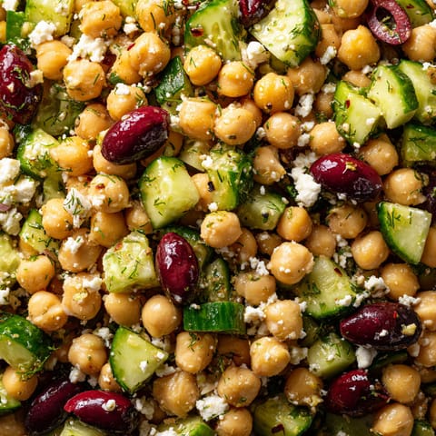 A close up of a salad with chickpeas, cucumbers, and olives.