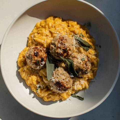 Warm, creamy pumpkin orzo surrounds flavorful sage turkey meatballs, a delightful family meal.