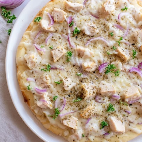 A close-up of a Chicken Alfredo Pizza, showing the perfectly browned crust and bubbly, cheesy toppings.