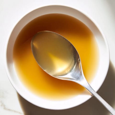 A strained, clear golden broth made from Vegetable Broth From Scraps poured into a glass jar, with a ladle and herb sprigs nearby on a rustic wooden table.  