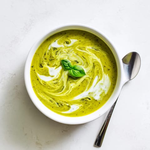 Creamy blended Courgette, Pea and Pesto Soup steaming in a white bowl, paired with a slice of crusty bread for dipping on the side.