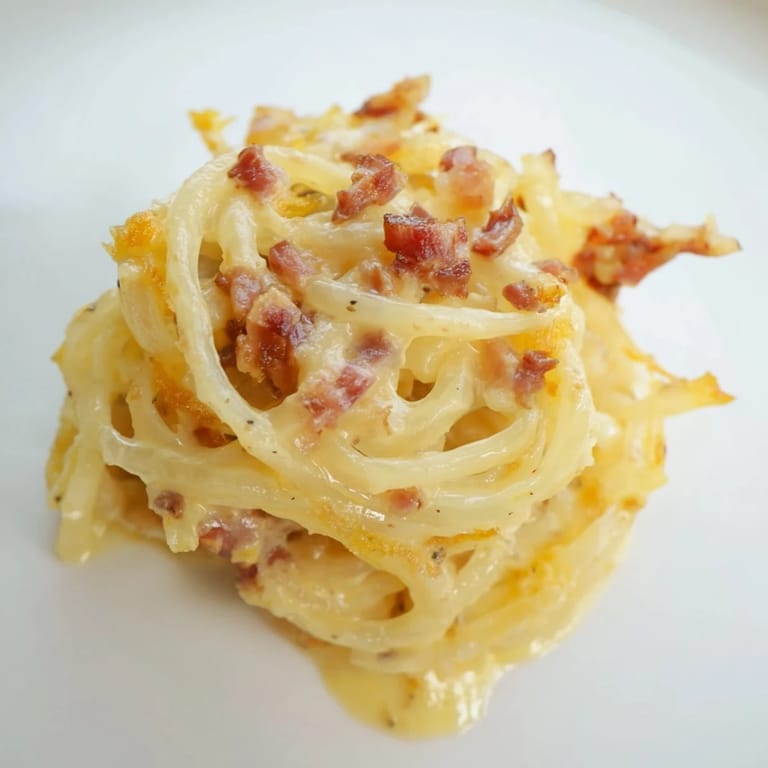 Close-up of celeriac carbonara, highlighting tender noodles coated in sauce with cracked black pepper.